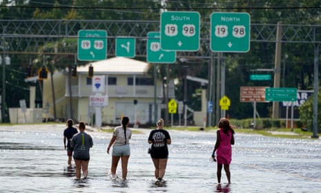 Four people walking through flood waters at their ankles in the middle of a street below freeway signs