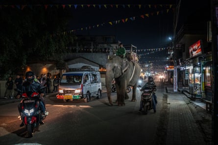 An elephant with a man riding on it among traffic