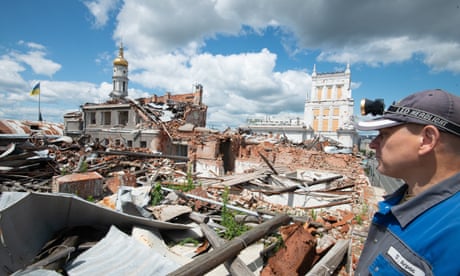 A man in overalls surveys ruined buildings and rubble
