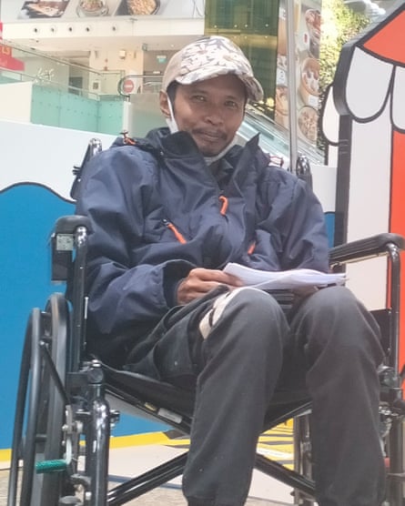 A man wearing a cap sits in a wheelchair holding papers.