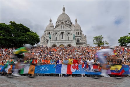 Riders race past spectators waiting outside Basilique du Sacré-Coeur de Montmartre.
