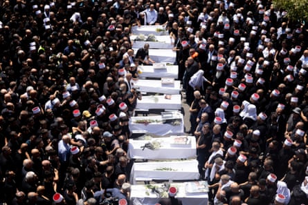 Hundreds of mourners grieve as ten white coffins proceed through a funeral