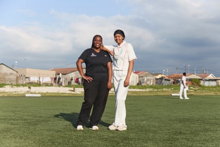 A tall African girl in cricketers' clothing stands next to an older woman in black shirt and trousers