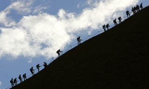 Tourists climb the monolith of Uluru