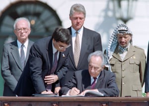 Peres signs the Oslo accords in a ceremony at the White House in Washington, DC, watched by (background L to R) Rabin, Bill Clinton and Arafat.