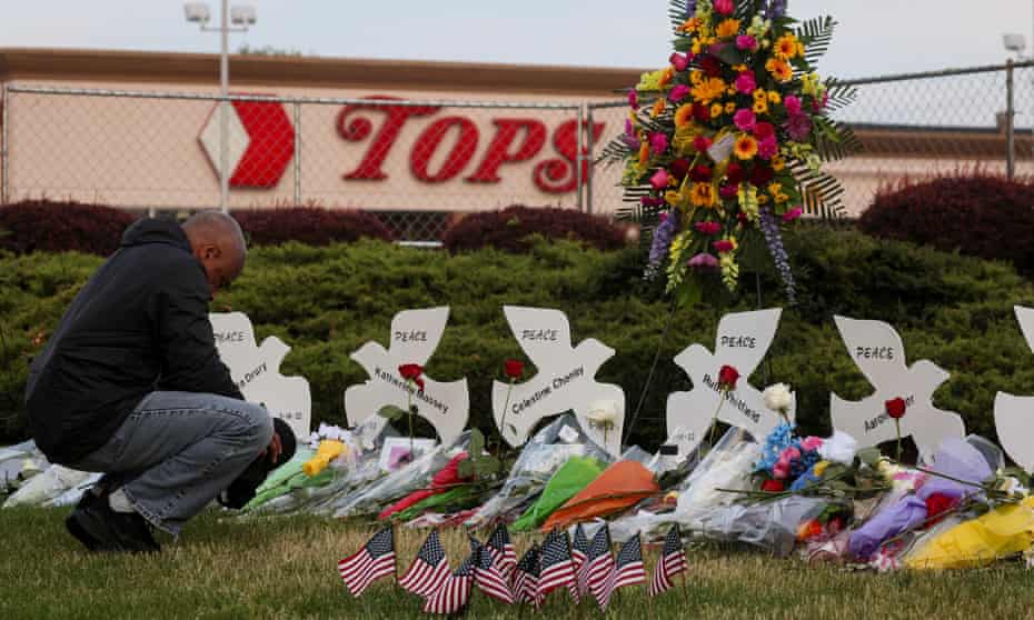 Man kneels next to cutouts of doves and bouquets of flowers outside Tops market