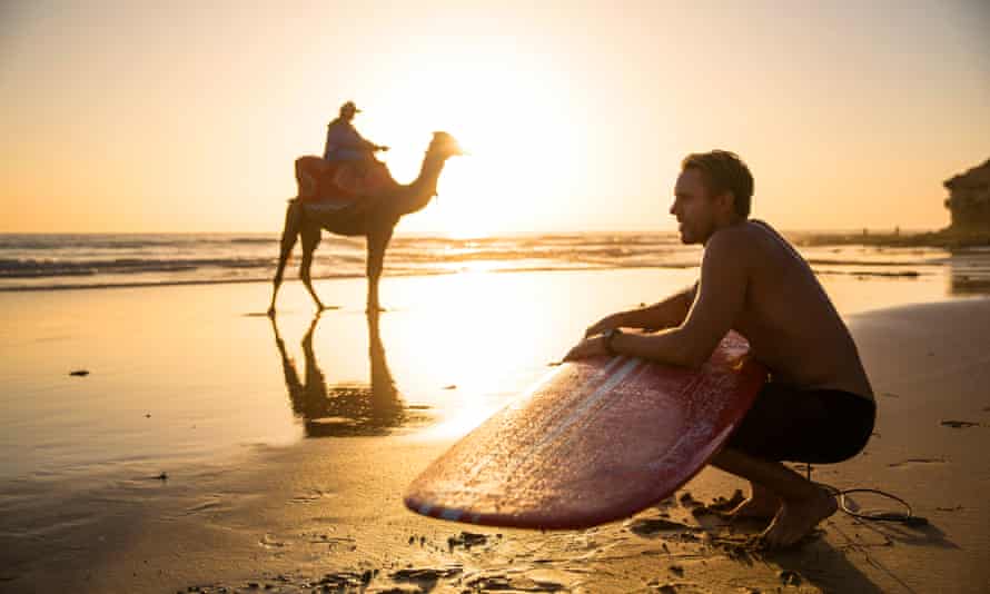 A surfer and a camel share the beach at Taghazout, Morocco.