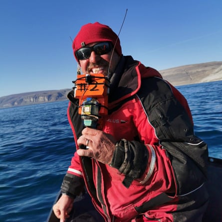 Greenland shark expert Nigel Hussey holds a sensor, on a boat wearing sunglasses and cold-weather gear.