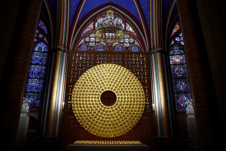 A striking wooden container featuring a large hammered metal circle on its front, set in a chapel with stainedf glass windows and a sky and stars ceiling