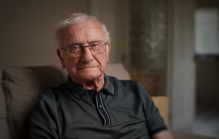 A man of age with grey hair, glasses and a dark grey collar-necked top