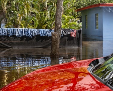 a perfect row of jeans laid out to dry while floodwater still filled the street below. The image feels symbolic, as if ordinary domestic life is being carefully reassembled on top of a shifting and uncertain ground. A small American flag hangs beside the denim, heightening the tension between everyday routine and the reality of a changing climate.’