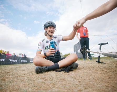 a woman in cycling lycra and a helmet sits on the ground and bumps fists with someone
