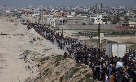 long column of displaced Palestinians walk next to a beach