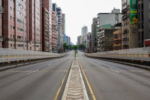 An empty four-lane road lined by a mixture of highrise and lowrise buildings