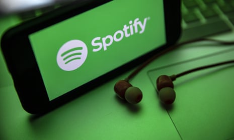 the Spotify logo seen displayed on a smartphone screen near a pair of earphones