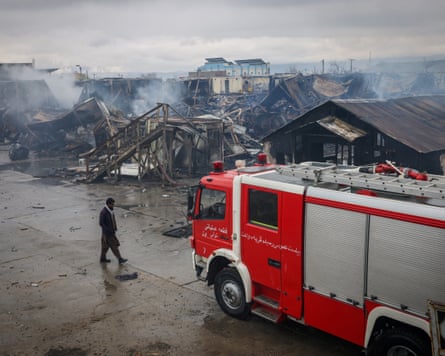 An man walks the smouldering remains of a drug rehabilitation centre with a red fire engine to his right