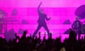 Jarvis Cocker performing on stage against a pink background with the crowd's raised hands silhouetted below