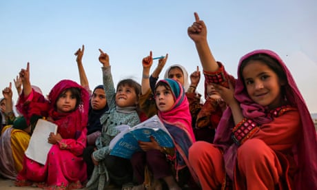 A group of school girls raise their hands with school books on their laps