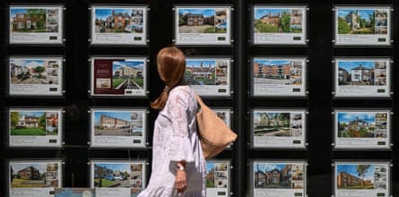 A woman looks at property listings posted in the window of an estate agent