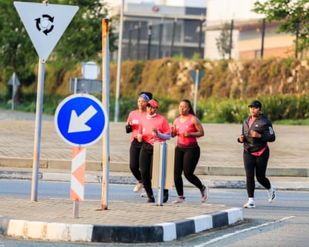 Four women in ink and black running gear run across a road