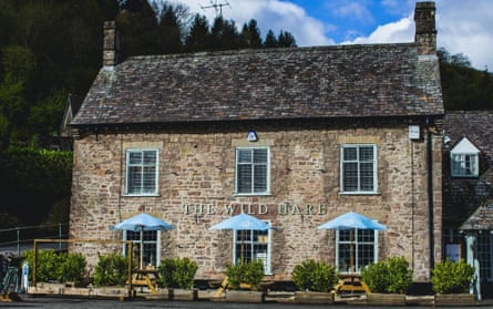 The exterior of the Wild Hare pub on a sunny day, it is a stone building with three tables outside
