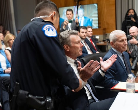 A police officer approaches David Schertler as he sits with his hands apart in a disbelieving gesture