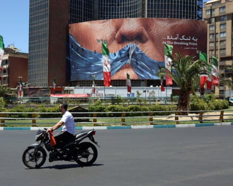 People drive in front of a large anti-US billboard in Tehran