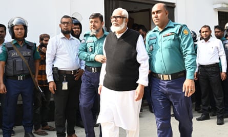 An older man with a grey beardbeing led by two men in uniform