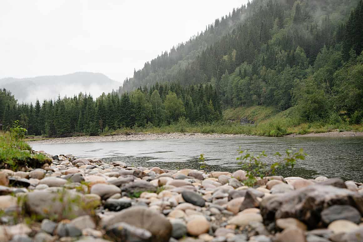A wide shot of the Gaula River in Norway, with forests and a mountain in the background.
