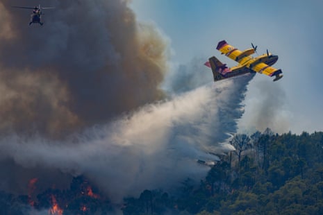 A Canadair water bomber drops water on a fast moving wildfire as a firefighting helicopter flies above the smoke near Cotignac, France.