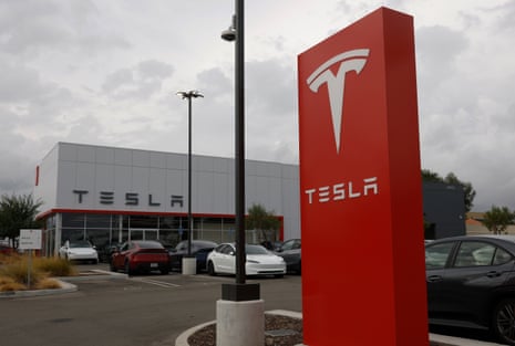 A large red Tesla sign stands in a car park outside a Santa Clarita Tesla dealership