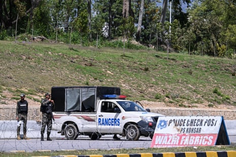 दो वर्दीधारी और हथियारबंद आदमी एक पुलिस चौकी पर रेंजर्स वाहन के बगल में खड़े हैं।