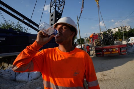 A construction worker drinks water to stay hydrated at a massive construction site as temperatures reached record highs in Paris last week