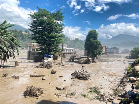Destroyed buildings and vehicles protrude from mud on a flooded street in Nepal.