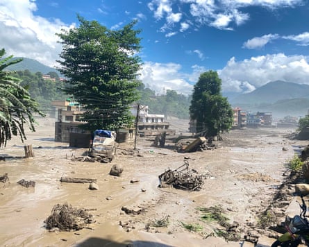 A drone view of damaged homes and vehicles partially submerged in a sea of mud