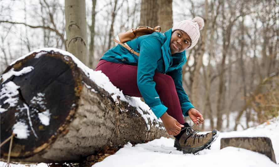 Camara Chambers sits on a a felled log in snow to put on her walking boots