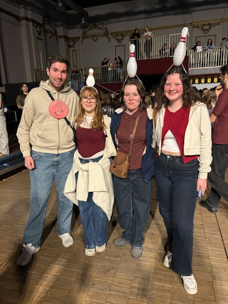 Three young women, each with a bowling pin attached to their head, standing next to a young man with a cardboard bowling ball stuck to his top