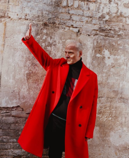 Mark Bonnar in a red coat with one arm up as if waving