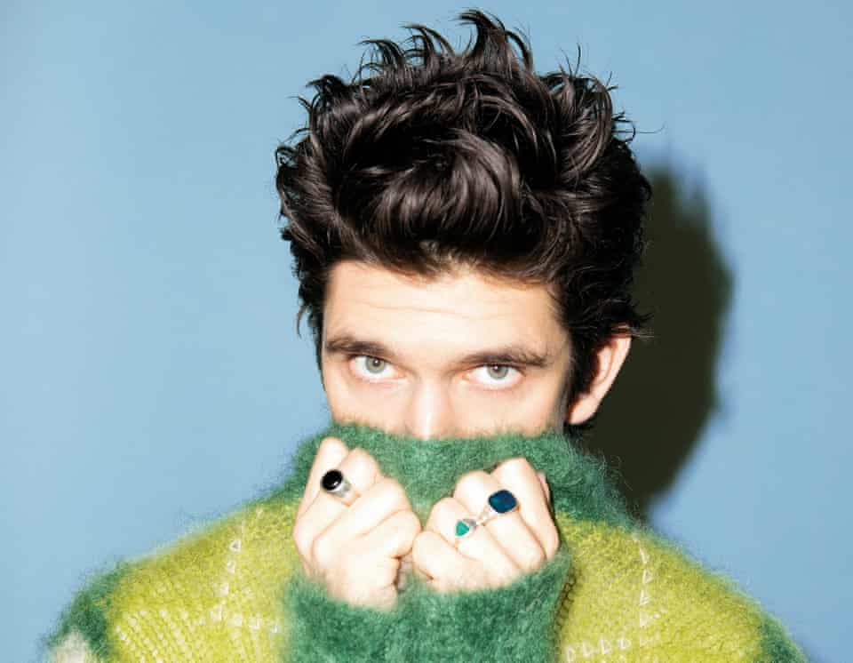 Head shot of actor Ben Whishaw in yellow and green jumper against blue background, January 2022