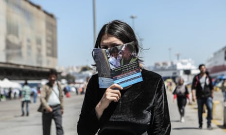 A woman hides her face behind an advice leaflet for refugees at the Piraeus passenger terminal in Athens.