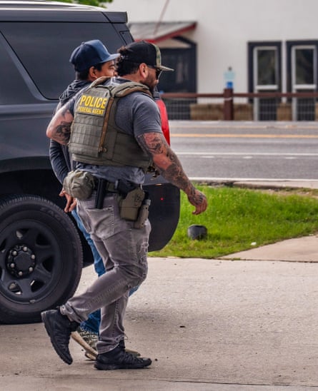 a man with tattoos and sunglasses in a vest that reads âÂÂPolice Federal Agentâ holds a man by the arm he takes him away in handcuffs