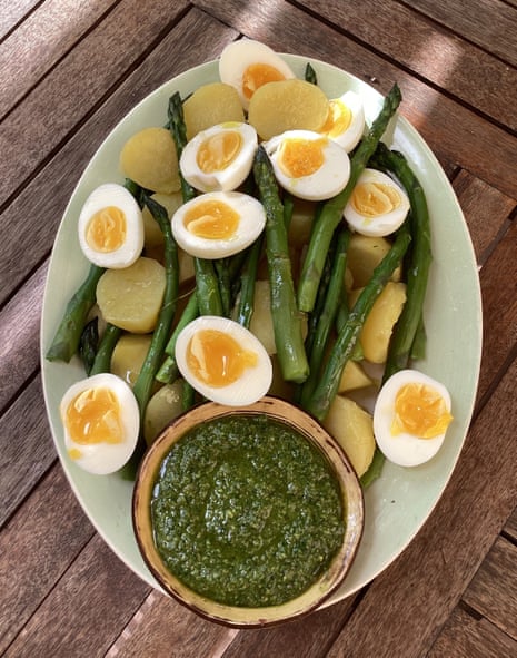 Rachel Roddy's potatoes under some halved boiled eggs sitting atop asparagus, and a pot of green sauce at the bottom of an oval plate.