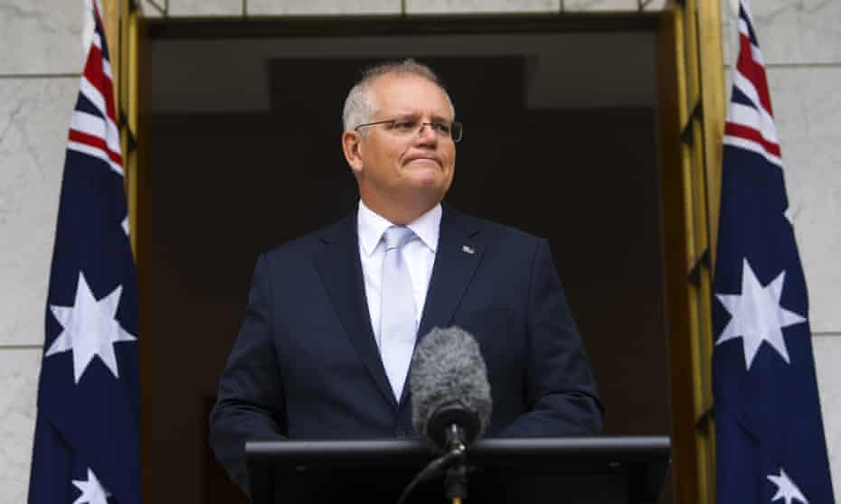 Scott morrison at a press conference standing at a lectern between two Australian flags