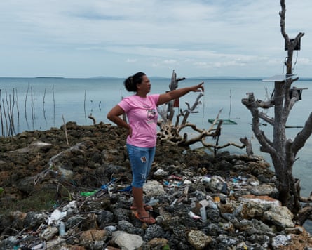 Trixy Elle points across the water on an island strewn with waste