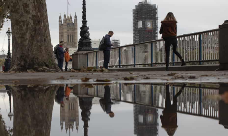 Members of the public are reflected in a puddle near the Houses of Parliament.