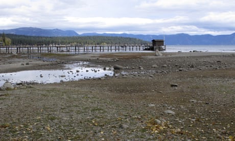 A dock sits above the receding shoreline of Lake Tahoe under a cloudy sky.