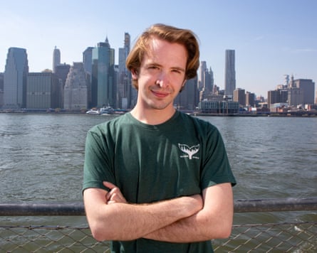 A young white man in a T-shirt poses against the New York skyline