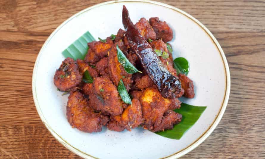 A round white plates with pieces of red/brown fried chicken with a whole dry-fried chill on top