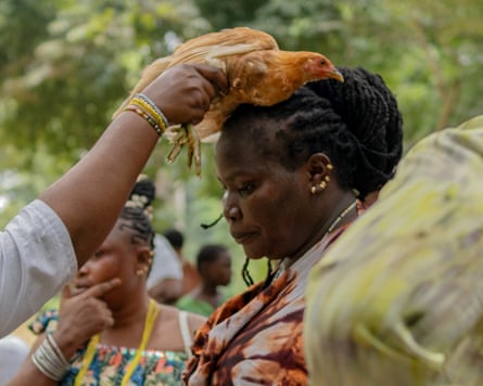 A woman with an extravagant hairstyle holds a chicken on the head of another woman