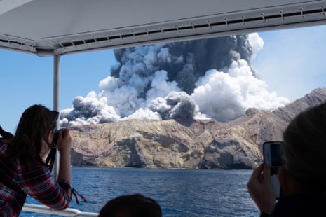 White Island (Whakaari) volcano erupts with clouds of ash, view from a boat with tourists taking pictures